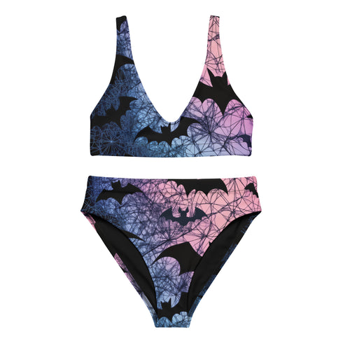 Model wearing a high-waisted pastel goth bikini set featuring a black bat and spiderweb print over an ombré pink and purple background. The two-piece swimsuit includes a scoop neck top and high-rise bottoms, styled outdoors in bright festival and poolside settings. Made of recycled fabric, soft, stretchy, and UV resistant. Available in XS to 3X. Aesthetic is gothic, spooky cute, and Y2K inspired.